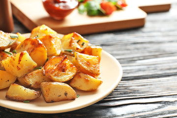 Plate with tasty potato wedges on wooden table
