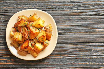 Plate with tasty potato wedges on wooden table