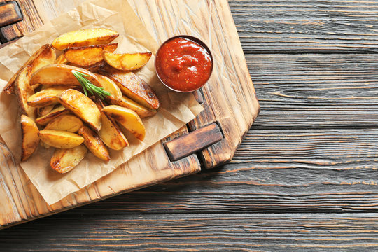 Wooden board with tasty potato wedges on table