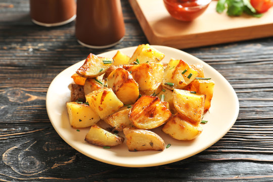 Plate with tasty potato wedges on wooden table