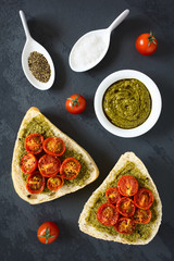 Olive bread roll halves spread with basil pesto and topped with roasted cherry tomato halves, photographed overhead on slate with natural light