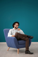 Handsome man sitting in comfortable armchair against color wall