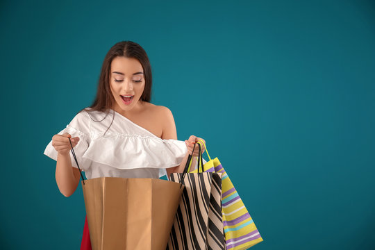 Surprised young woman looking inside of shopping bag on color background