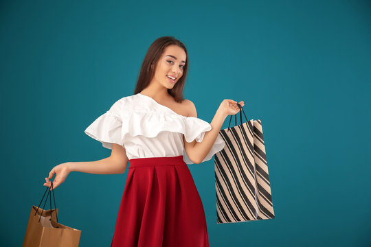 Beautiful young woman with shopping bags on color background