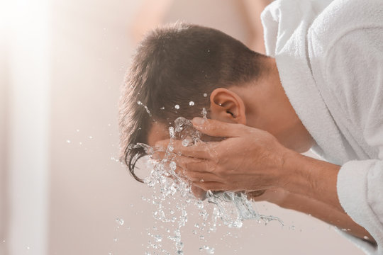 Man spraying water on his face after shaving in bathroom