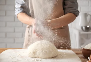 Fotobehang Woman clapping and sprinkling flour over dough on table © Africa Studio