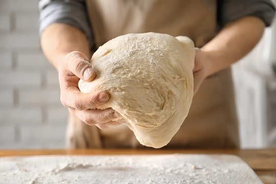 Woman holding dough above table sprinkled with flour