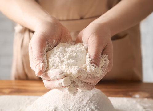 Woman holding wheat flour above dough on table, closeup