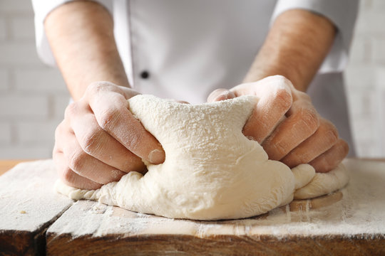Man kneading dough on wooden board sprinkled with flour