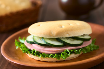 Sandwich aus Chilenischem Hallulla Brötchen belegt mit Salatblatt, Aufschnitt und Gurke, fotografiert mit natürlichem Licht (Selektiver Fokus, Fokus auf die Vorderseite des Sandwichs)