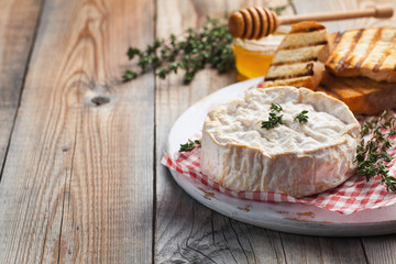 A real Camembert from France with thyme, honey and toasted bread on old wooden rustic table. Soft cheese on a wooden background with copy space