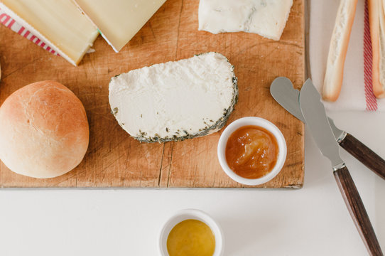 Wooden cheese plate with Italian Gorgonzola cheese, French farmer cheese or formage frais, organic European hard cheese, freshly baked bun, Italian bread sticks Grissini and mustard and fig jam