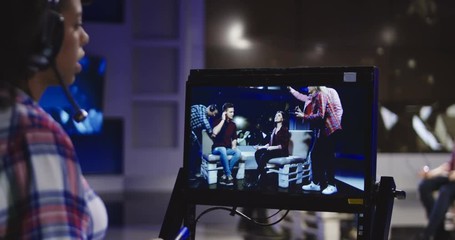 Casual African-American woman in headset controlling process of shooting TV show standing in front of computer screen and watching record.
