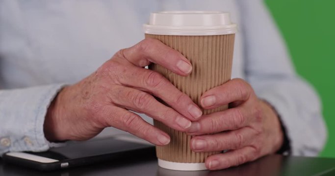 Close up of elderly person's hands grabbing coffee cup on green chroma key