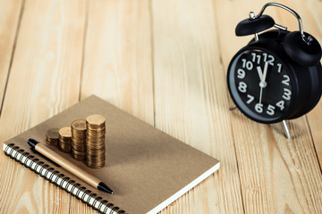 Steps of coins stack with vintage alarm clock and pen, notebook paper on wooden working table with copy space for text, financial and business planning concept. vintage tone.