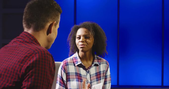 Casual multiethnic man and woman having discussion while sitting in telecasting studio and performing online show.