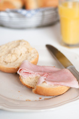 Breakfast table with sliced German kaiser roll or Austrian Vienna roll with butter and cooked ham with bread basked and glass of orange juice in background