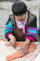 Senior Chukchi woman cuts  just catched sallmon on the sea shore and prepared it for drying