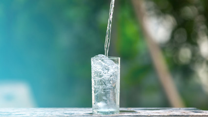 Drink water pouring in to glass over sunlight and natural green background.Select focus blurred...