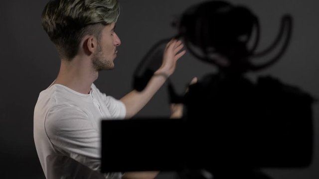 Happy confident young man filming himself in a professional studio and talking to camera
