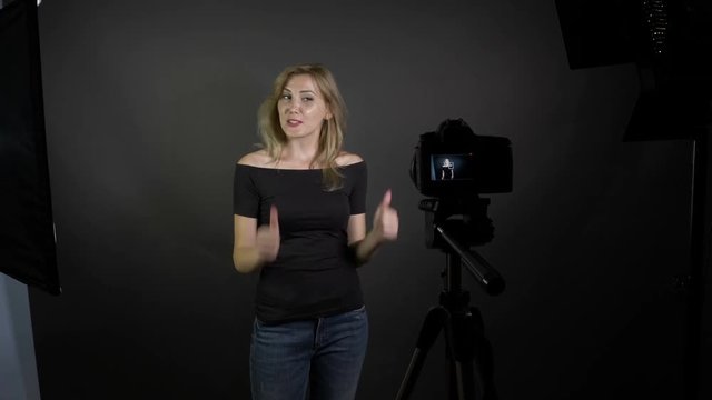 Young smiling blonde female blogger recording vlog message for her subscribers in a professional studio
