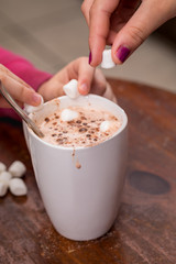 Two people putting marshmallows in a cup of hot chocolate