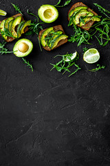 Snacks with avocado. Avocado toast with rye bread on black background top view copy space