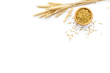 Raw oats in bowl near sprigs of wheat on white background top view copy space