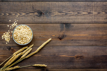 Cereals concept. Oatmeal in bowl near sprigs of wheat on dark wooden background top view copy space