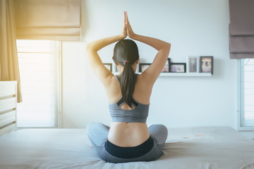 Young asian woman sitting on bed practicing doing yoga exercise,Female workout after waking up at home,Healthy and  lifestyle concept