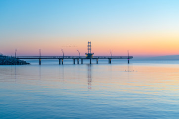 Birds flying over modern pier during pastel colored sunrise