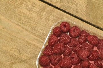 Red-fruited raspberries in plastic box on wooden background. Raspberries background. Close-up