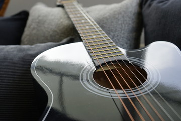 six stringed acoustic guitar on grey sofa