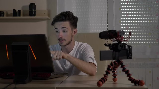 Young male video vlogger filming himself with a camera at office teaching audience how to start an online blog