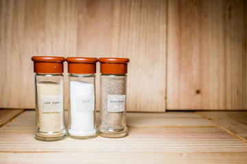 Concept of salt, black and white pepper powder accessories. Bottles with salt, black and white pepper on wooden background. Horizontal.