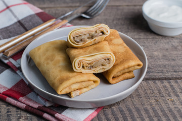 Russian Puncake Crepes stuffed with mushrooms and mozzarella on wooden table background.