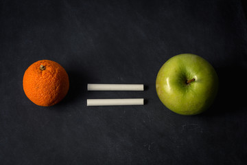 Orange equals apple with chalk on top of chalkboard suggesting equality in different fruit