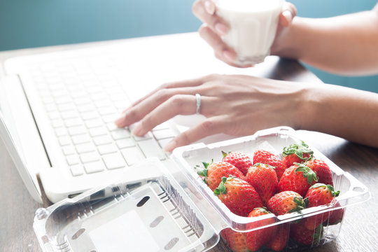 Fresh strawberries on office desk with woman drinking milk, Healthy concept