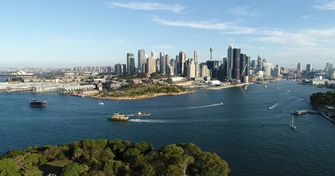 From Goat island green trees towards Barangaroo urban high-rise towers in Sydney city CBD over heavy boat traffic on Harbour.
