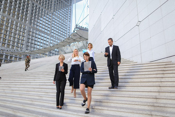 Employees of large  corporation walking in   and speaking by smartphone. Concept of successful business partners outside. Young prosperous people dressed in black suits look happy. © sisterspro