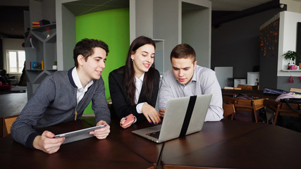 Three modern people, beautiful woman and two young men chatting and using laptop call classmate in...