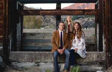 A young family of three sitting on an old concrete wal surround by old rustic wood for a family portrait