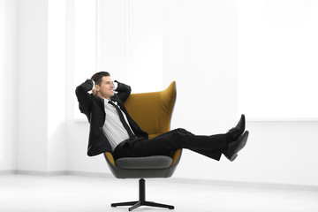 Handsome businessman sitting in comfortable armchair indoors