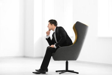 Handsome businessman sitting in comfortable armchair indoors
