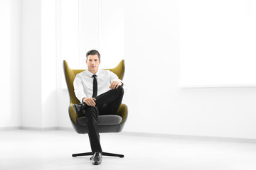 Handsome businessman sitting in comfortable armchair indoors