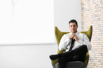 Handsome businessman sitting in comfortable armchair indoors