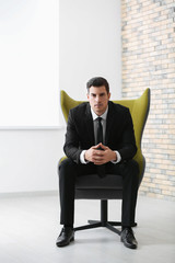 Handsome businessman sitting in comfortable armchair indoors