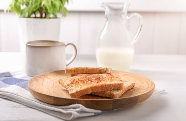 Wooden plate with tasty toasted bread and cup of coffee on table