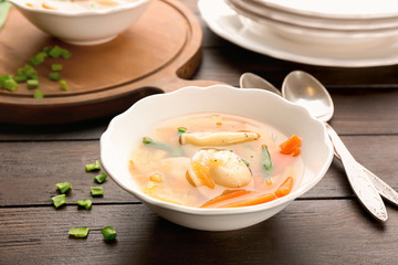 Tasty broth with dumplings on wooden table