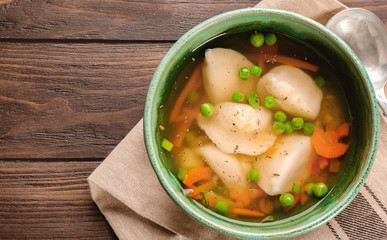 Tasty broth with dumplings on wooden table
